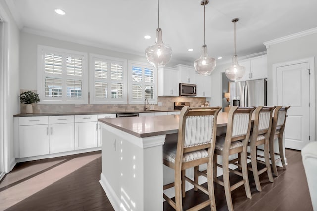 kitchen featuring dark hardwood / wood-style flooring, stainless steel appliances, pendant lighting, a center island, and white cabinetry