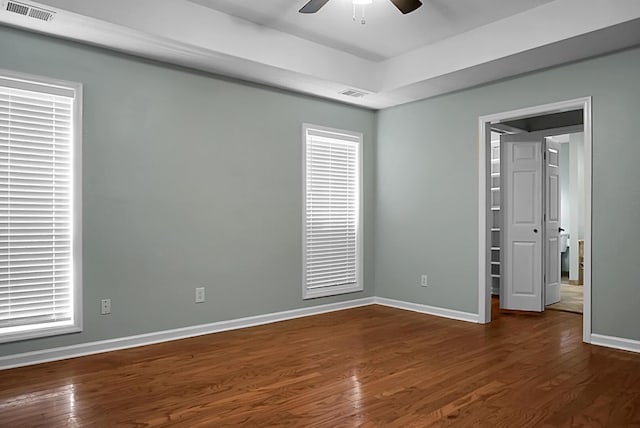 unfurnished room with a raised ceiling, ceiling fan, and dark wood-type flooring