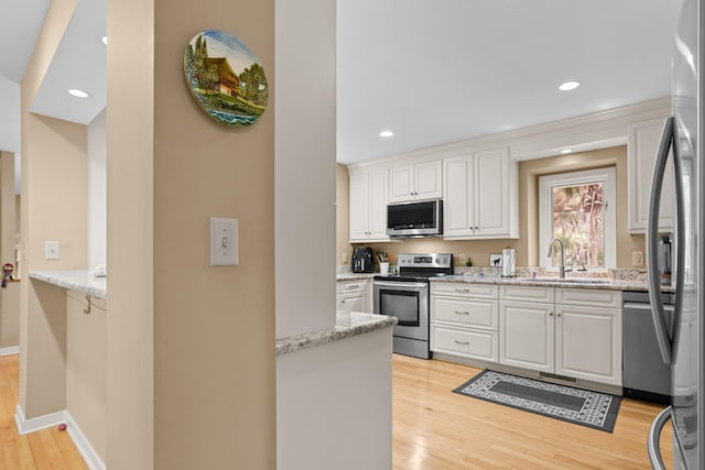 kitchen featuring stainless steel appliances, white cabinetry, light stone countertops, and sink