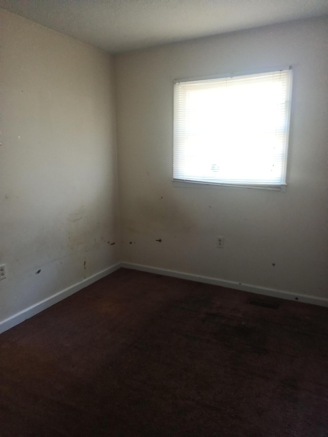 unfurnished room with visible vents, baseboards, and dark carpet