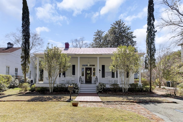 view of front of home with a front lawn, a chimney, covered porch, and metal roof