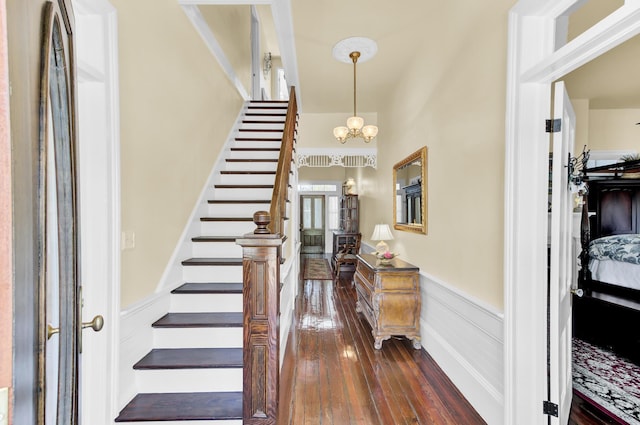 entrance foyer with stairs, an inviting chandelier, dark wood-style flooring, and wainscoting