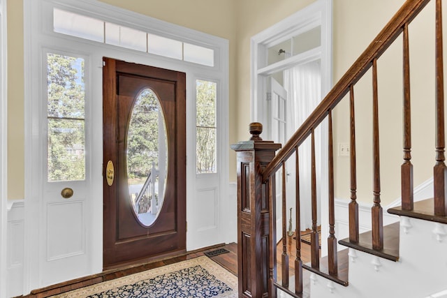 foyer entrance with stairway, a decorative wall, wood finished floors, and wainscoting