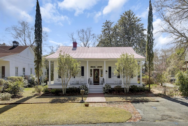 view of front of property featuring a front yard, a chimney, covered porch, and metal roof