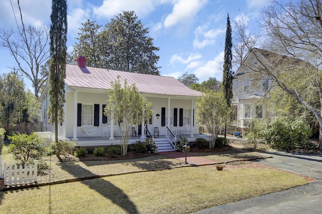 view of front of home with a front yard, a standing seam roof, a porch, a chimney, and metal roof