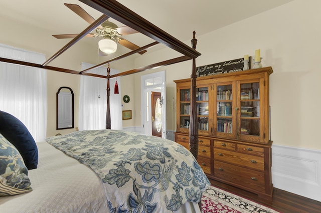 bedroom with wood finished floors, a decorative wall, a ceiling fan, and wainscoting