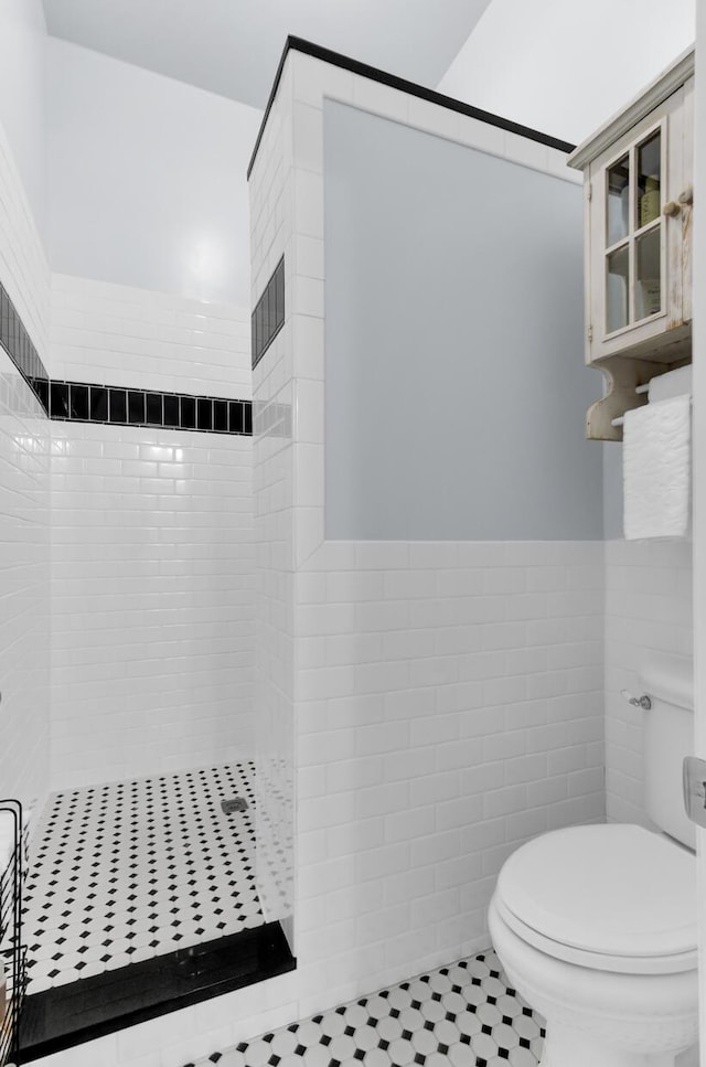 full bathroom featuring a tile shower, a wainscoted wall, toilet, and tile walls