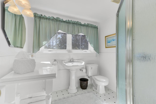 bathroom featuring toilet, visible vents, a shower with door, and wainscoting