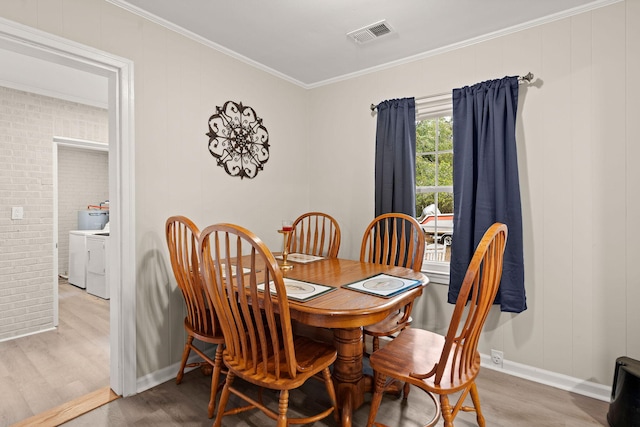 dining space featuring hardwood / wood-style flooring, washing machine and clothes dryer, ornamental molding, and brick wall