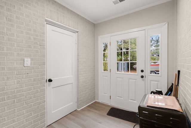 foyer with crown molding, light hardwood / wood-style floors, and brick wall