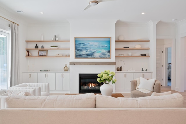 living area with built in shelves, a glass covered fireplace, visible vents, and crown molding