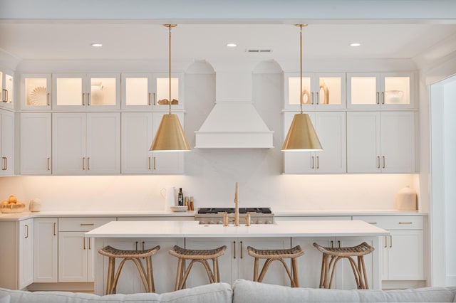 kitchen with light countertops, premium range hood, visible vents, and an island with sink