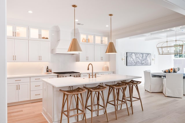 kitchen with light wood finished floors, light countertops, custom range hood, visible vents, and a kitchen island with sink