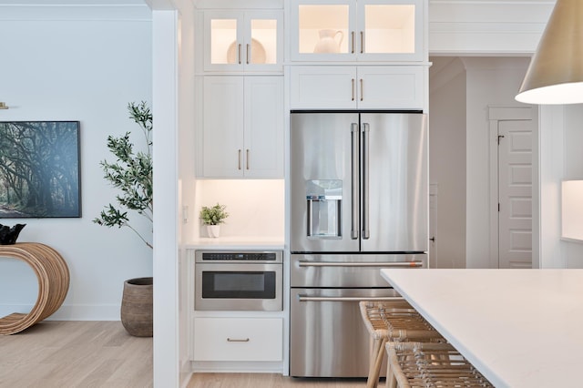 kitchen featuring white cabinets, glass insert cabinets, appliances with stainless steel finishes, light countertops, and light wood-type flooring