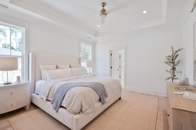 bedroom featuring light wood finished floors, baseboards, visible vents, and a raised ceiling