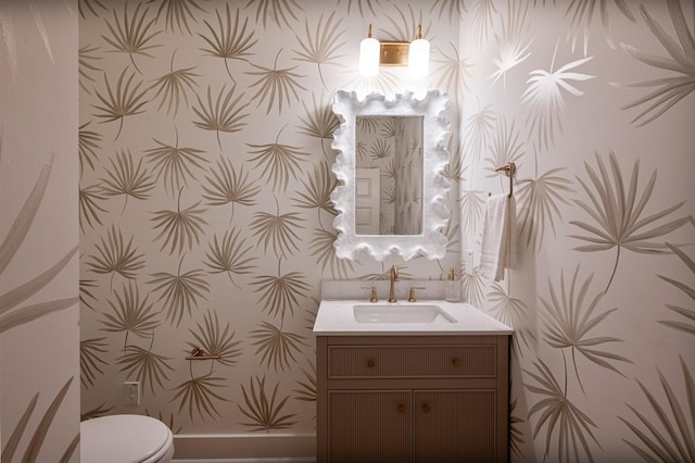 half bathroom with toilet, vanity, and wallpapered walls