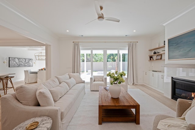 living room featuring ornamental molding, a glass covered fireplace, a ceiling fan, and recessed lighting