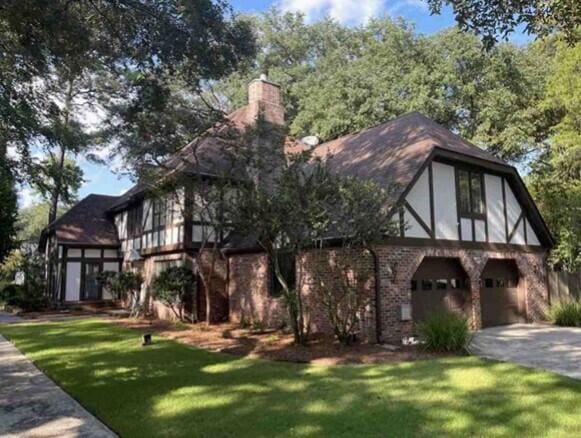 english style home featuring an attached garage, driveway, a chimney, and a front lawn