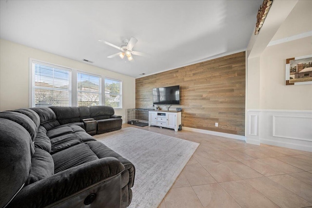 living room featuring visible vents, a ceiling fan, wooden walls, light tile patterned floors, and an accent wall