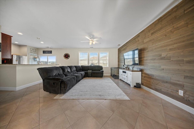 living room with wooden walls, light tile patterned flooring, a ceiling fan, and baseboards