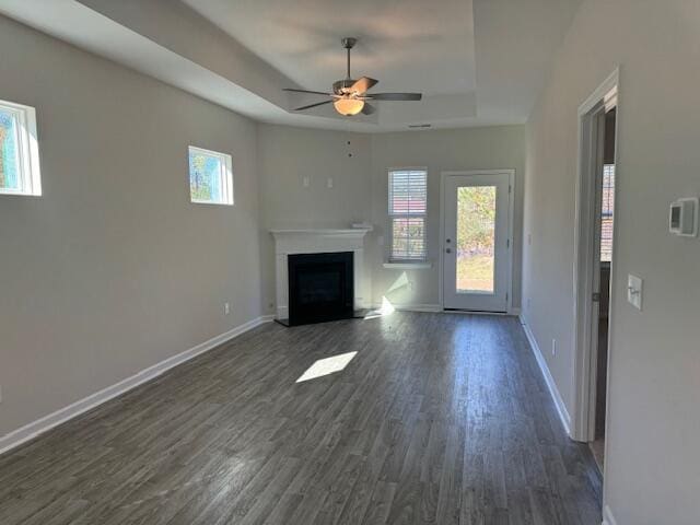 unfurnished living room featuring a tray ceiling, ceiling fan, and dark hardwood / wood-style flooring