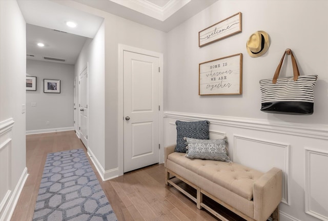 sitting room featuring wood finished floors, baseboards, recessed lighting, wainscoting, and a decorative wall