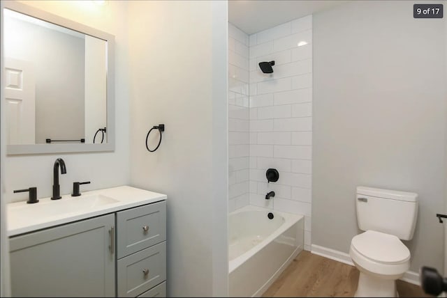 bathroom featuring toilet, wood finished floors, shower / bathing tub combination, baseboards, and vanity