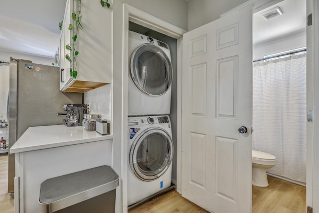 clothes washing area featuring visible vents, stacked washer and clothes dryer, laundry area, and light wood finished floors