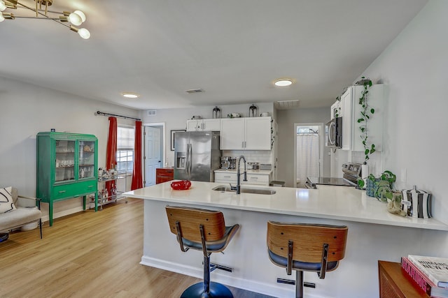 kitchen featuring visible vents, a sink, white cabinetry, stainless steel appliances, and a peninsula