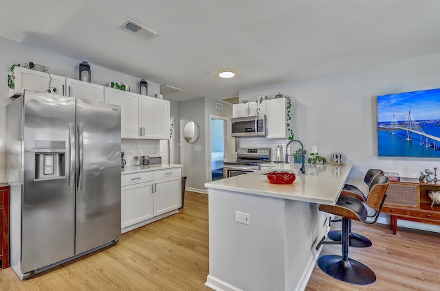 kitchen featuring a peninsula, a kitchen breakfast bar, white cabinets, stainless steel appliances, and a sink