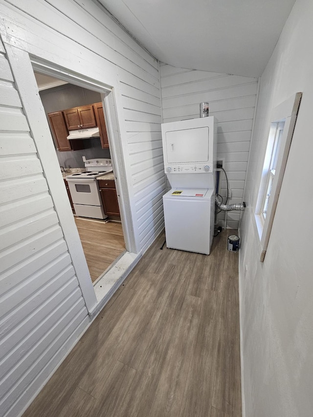 laundry area with stacked washer and dryer, wooden walls, and light hardwood / wood-style floors