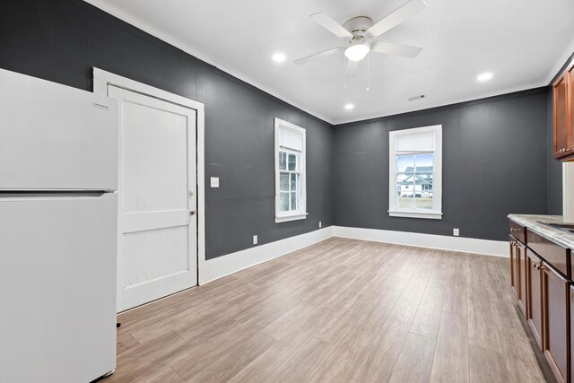 unfurnished dining area featuring ceiling fan, crown molding, and light wood-type flooring