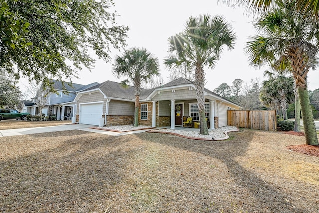 view of front of house with driveway, a garage, stone siding, fence, and a porch