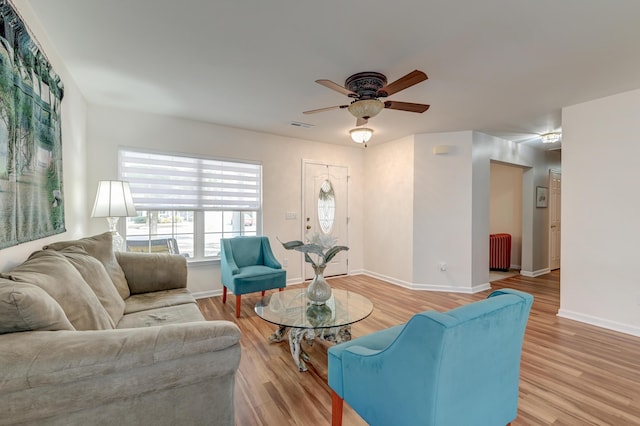 living room with radiator, light wood-style floors, visible vents, and baseboards