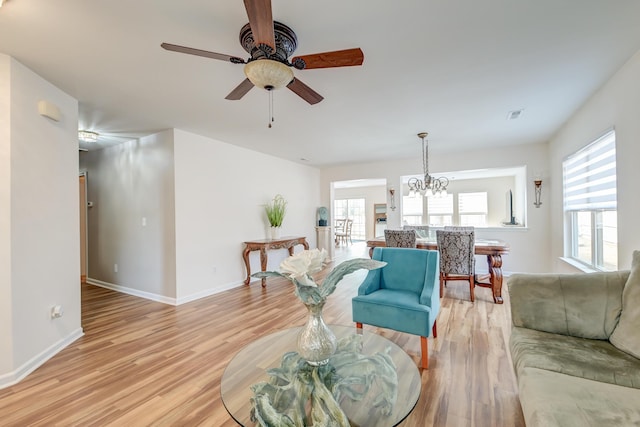 living area featuring ceiling fan with notable chandelier, visible vents, light wood-style flooring, and baseboards