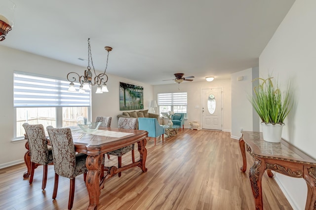 dining room with light wood-style flooring, baseboards, and ceiling fan with notable chandelier