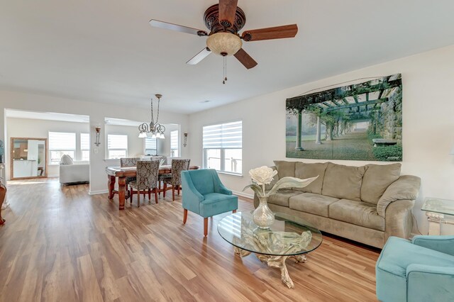 living area with baseboards, wood finished floors, and ceiling fan with notable chandelier