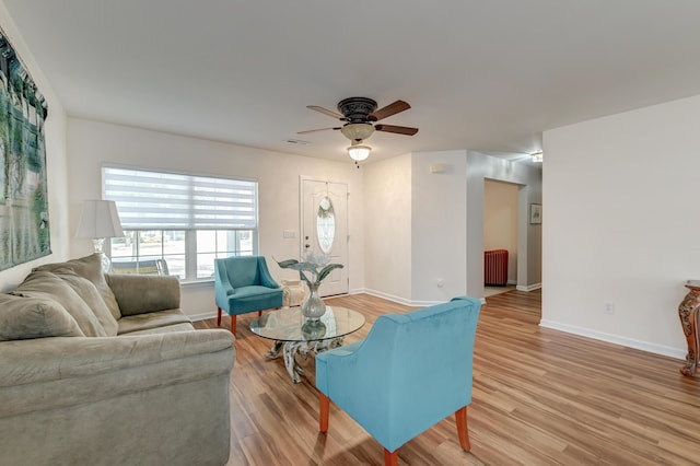 living area with a ceiling fan, light wood-type flooring, radiator, and baseboards