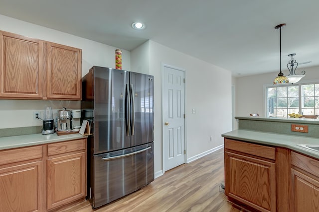 kitchen featuring baseboards, light countertops, freestanding refrigerator, light wood finished floors, and pendant lighting