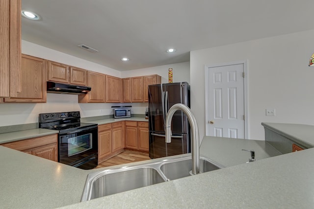 kitchen featuring black range with electric cooktop, under cabinet range hood, visible vents, freestanding refrigerator, and stainless steel microwave