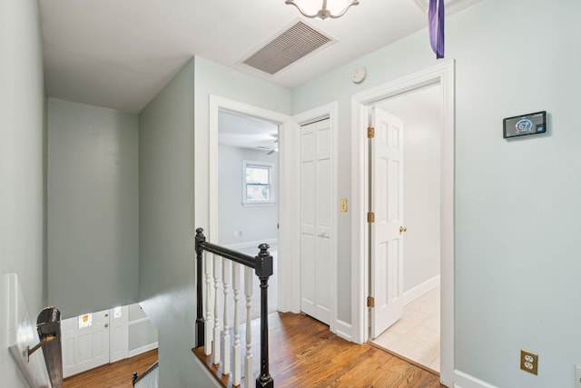 hall with baseboards, visible vents, wood finished floors, and an upstairs landing