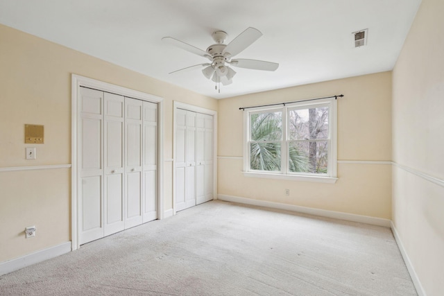 unfurnished bedroom with ceiling fan, light carpet, visible vents, baseboards, and two closets