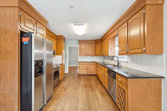 kitchen with appliances with stainless steel finishes, a sink, light wood-style flooring, and decorative backsplash