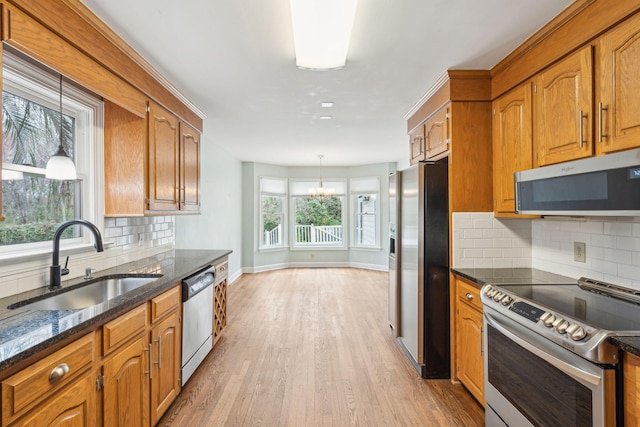 kitchen with pendant lighting, stainless steel appliances, light wood-style flooring, brown cabinetry, and a sink