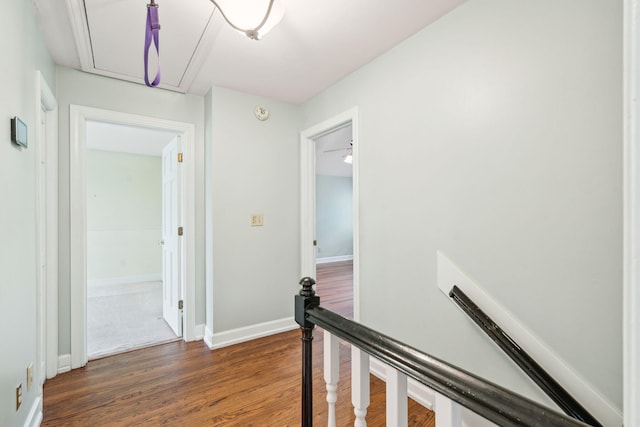 hallway with attic access, baseboards, dark wood-type flooring, and an upstairs landing