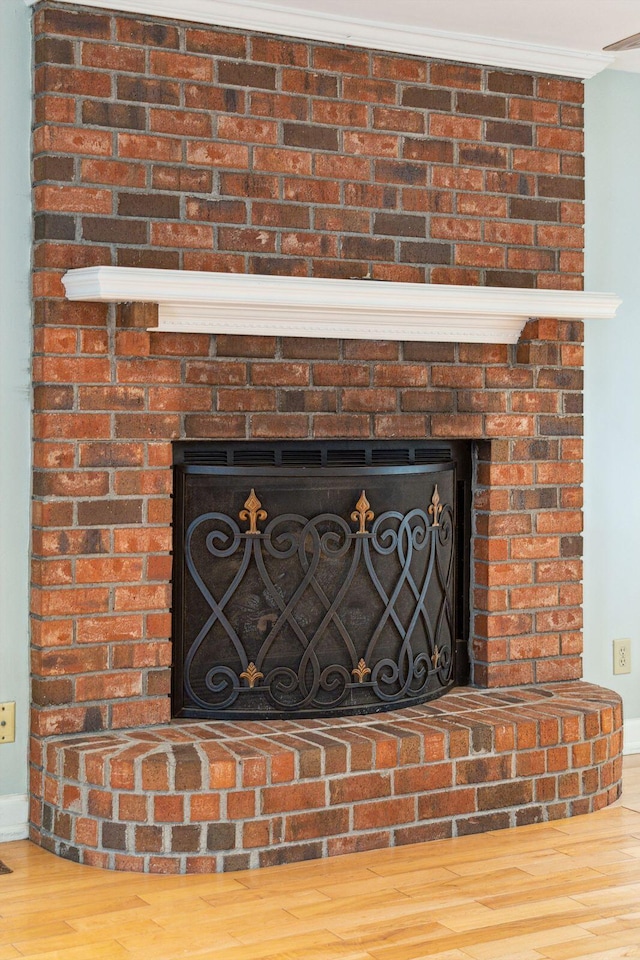 interior details with a brick fireplace, wood finished floors, and crown molding