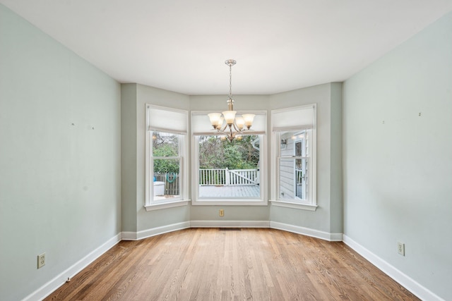 unfurnished room with an inviting chandelier, baseboards, and wood finished floors