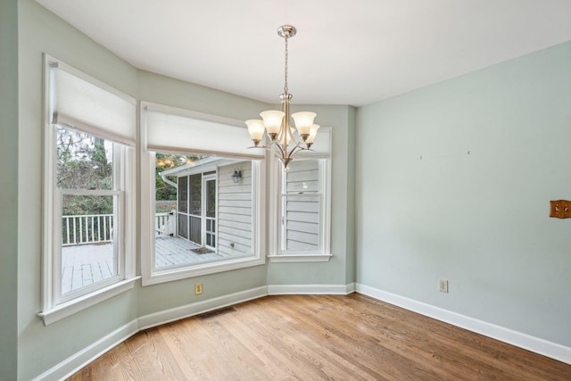 unfurnished dining area with a chandelier, visible vents, baseboards, and wood finished floors