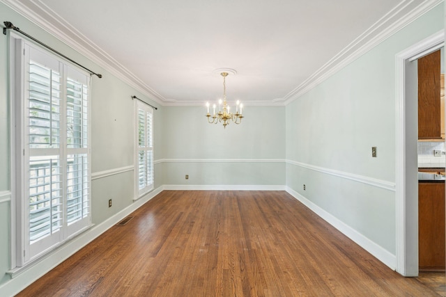 unfurnished room featuring a notable chandelier, wood finished floors, visible vents, baseboards, and crown molding