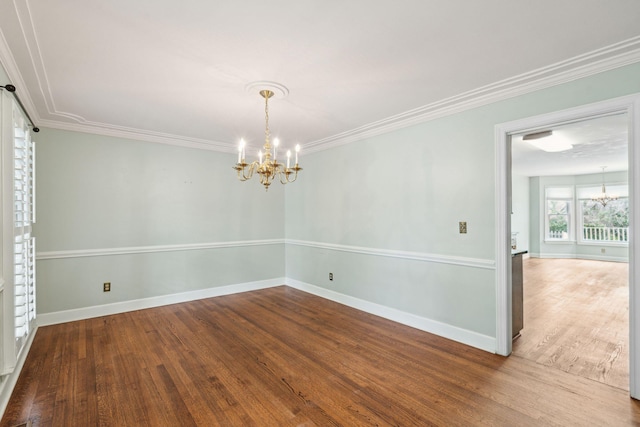 spare room with baseboards, crown molding, wood finished floors, and an inviting chandelier